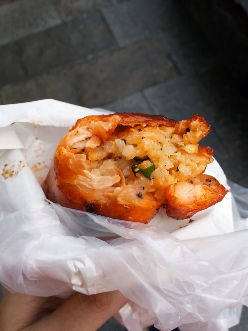 A close-up of a person holding a partially eaten food wrapped in a white paper bag.